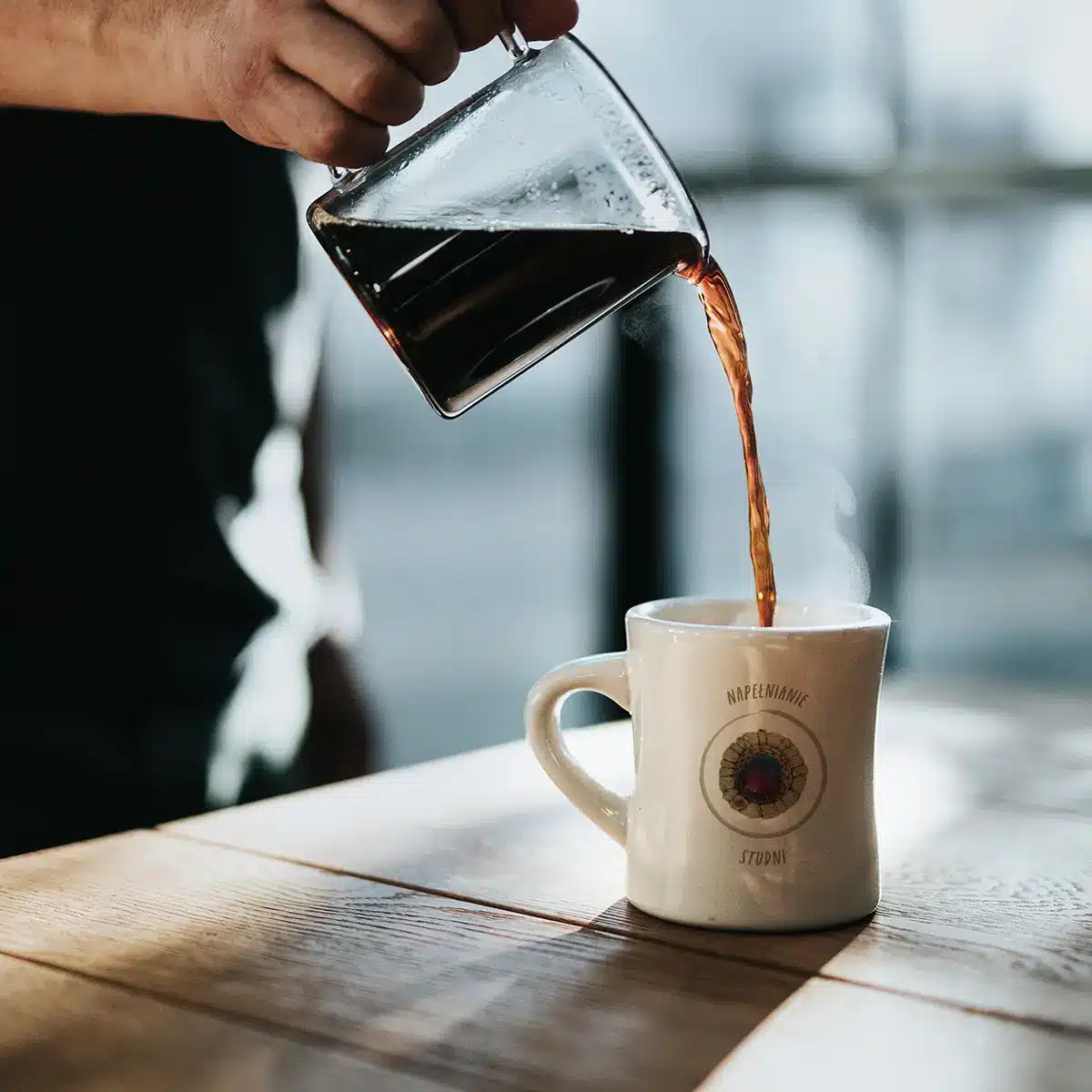 A person pouring a coffee into a white mug