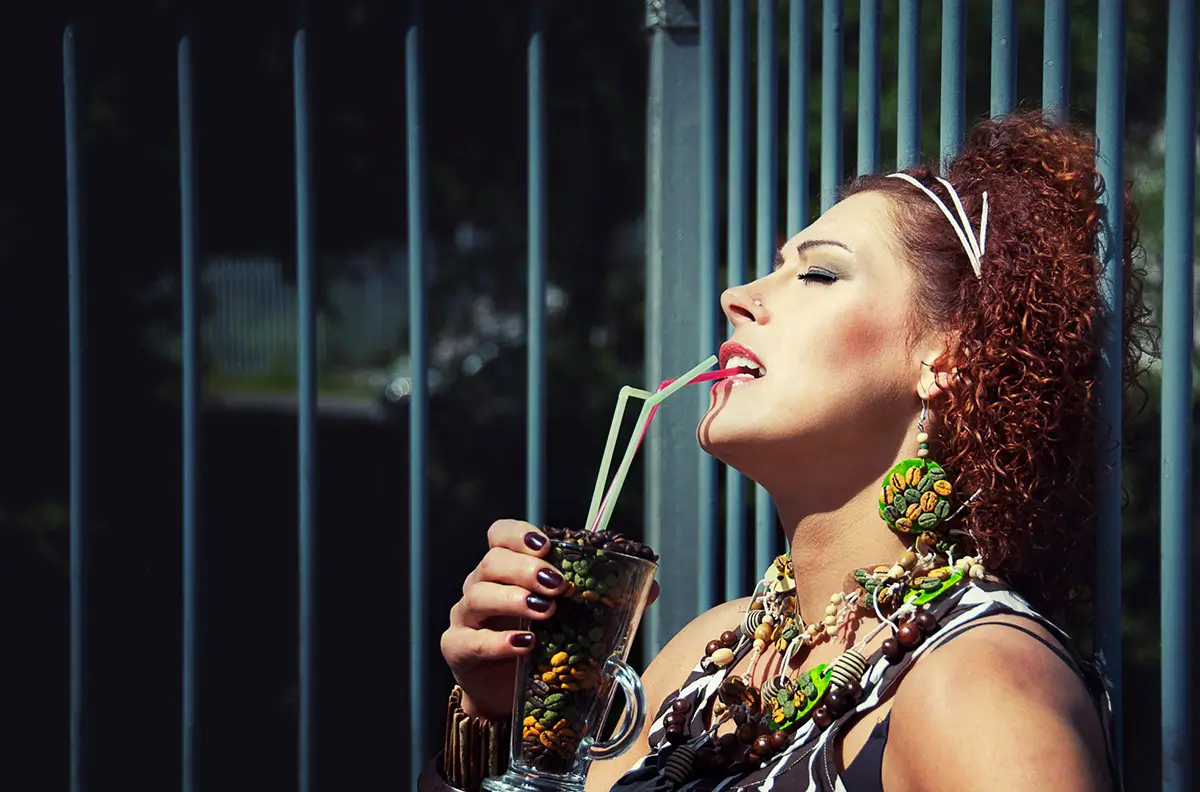 Woman holding a straw in her mouth, holding a glass full of coffee beans