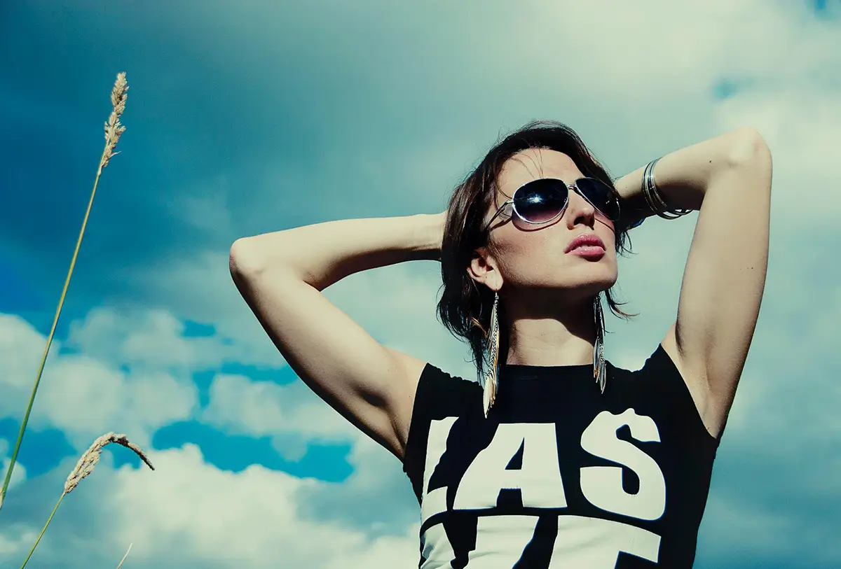 Portrait of a girl in sunglasses with her hands behind her head, blue sky in the background