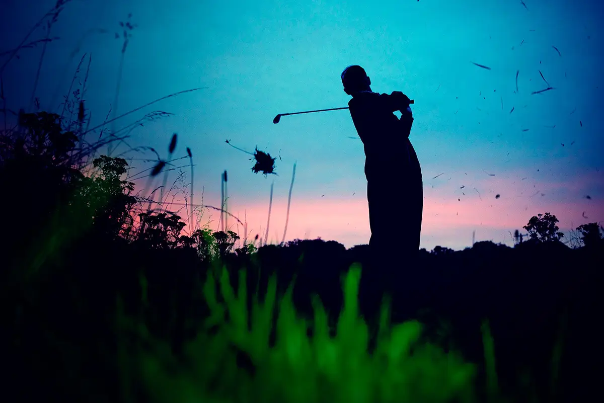 Silhouette of a man playing golf, sunset behind